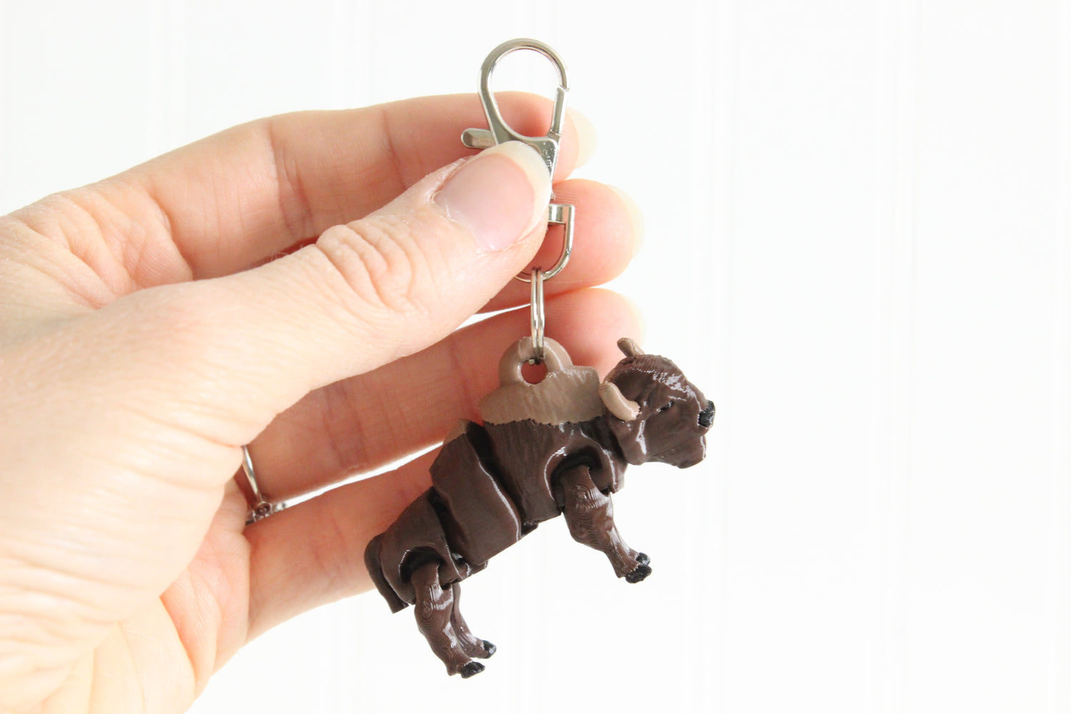 Hand holding 3D-printed brown bison keychain to show its size, colors, and silver swivel clip.