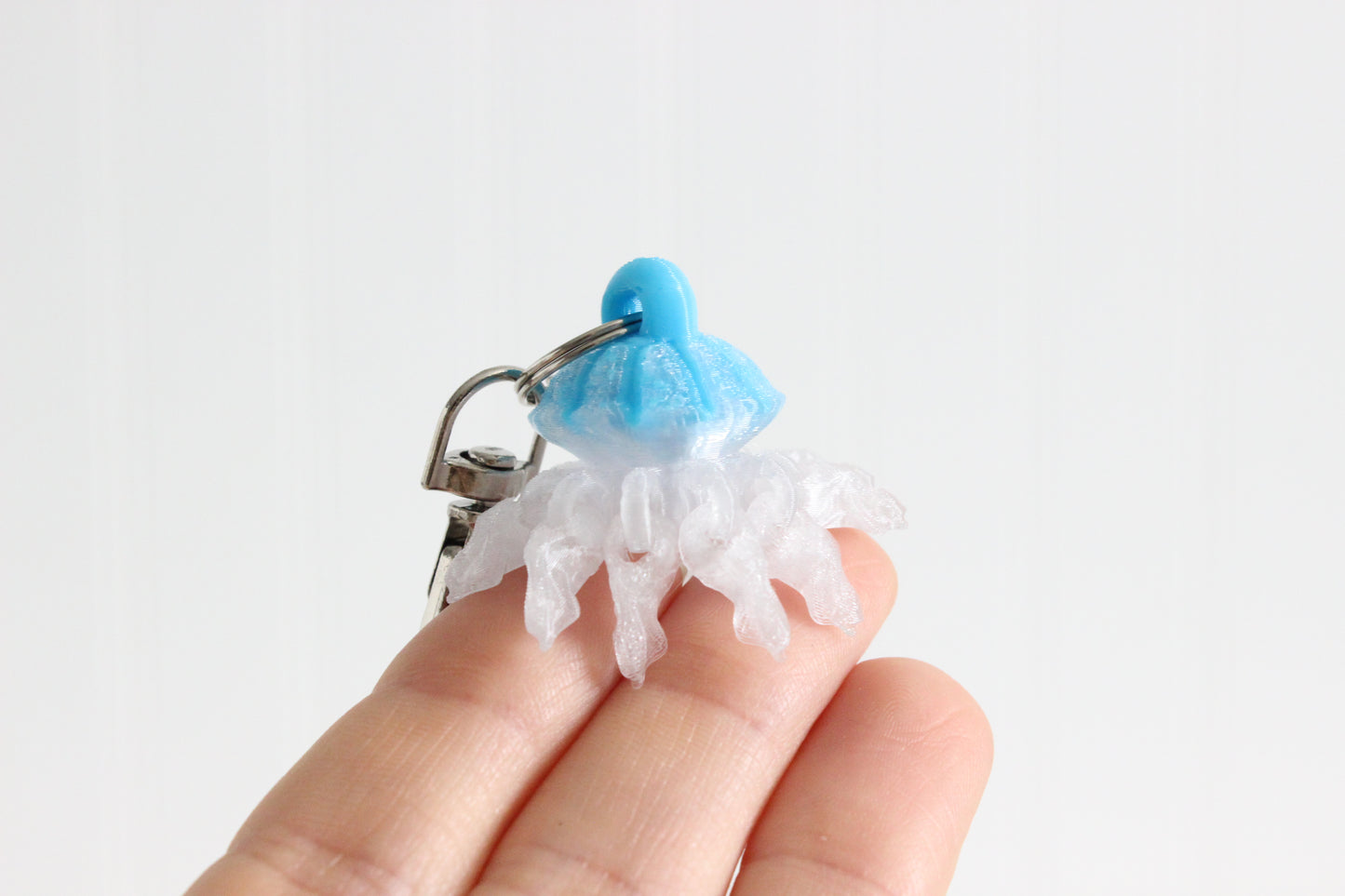 Hand holding the 3D-printed jellyfish keychain to show its size, colors, and silver swivel clip.