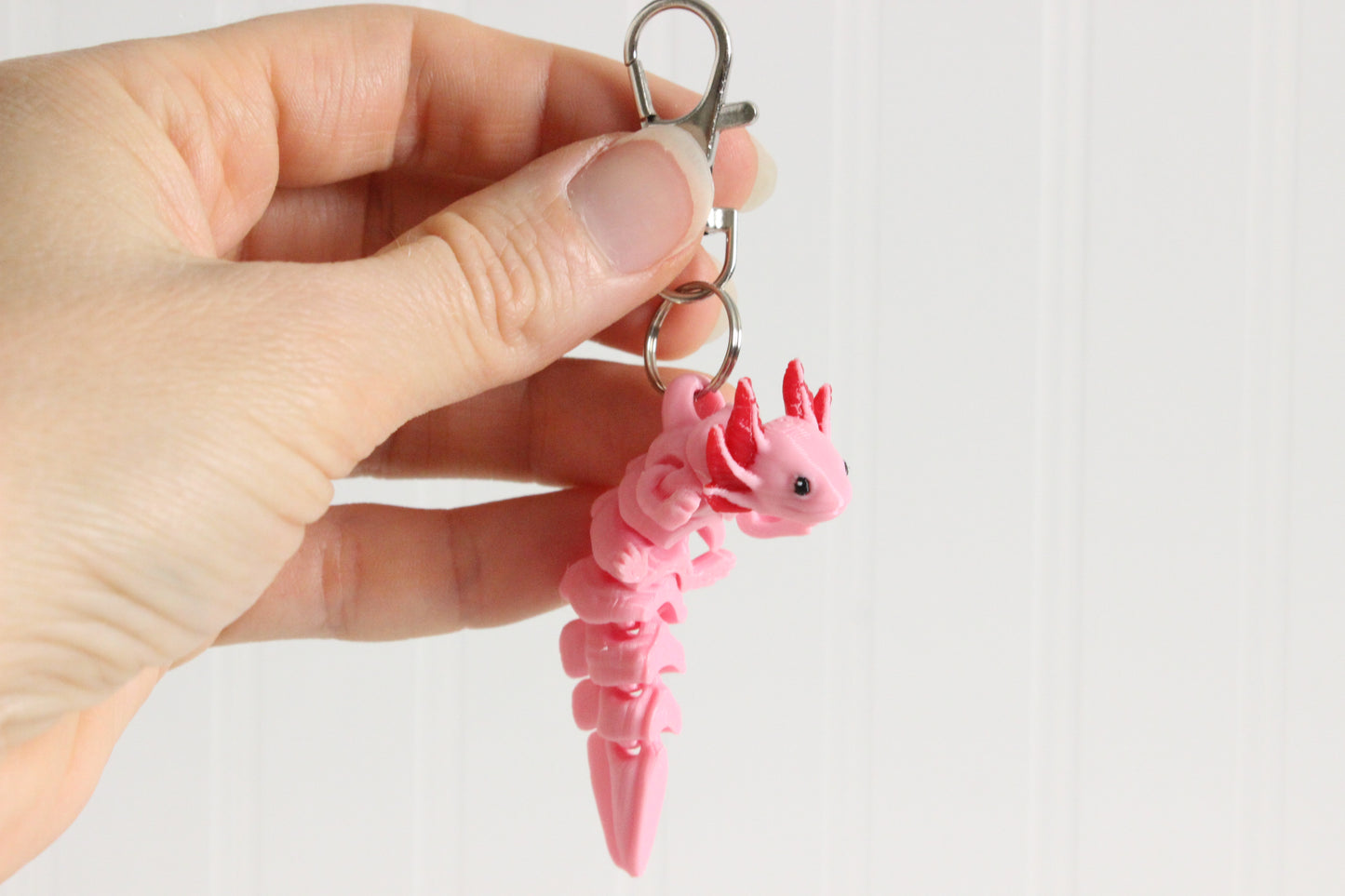Hand holding a pink 3D-printed axolotl keychain to show its size and external gills.