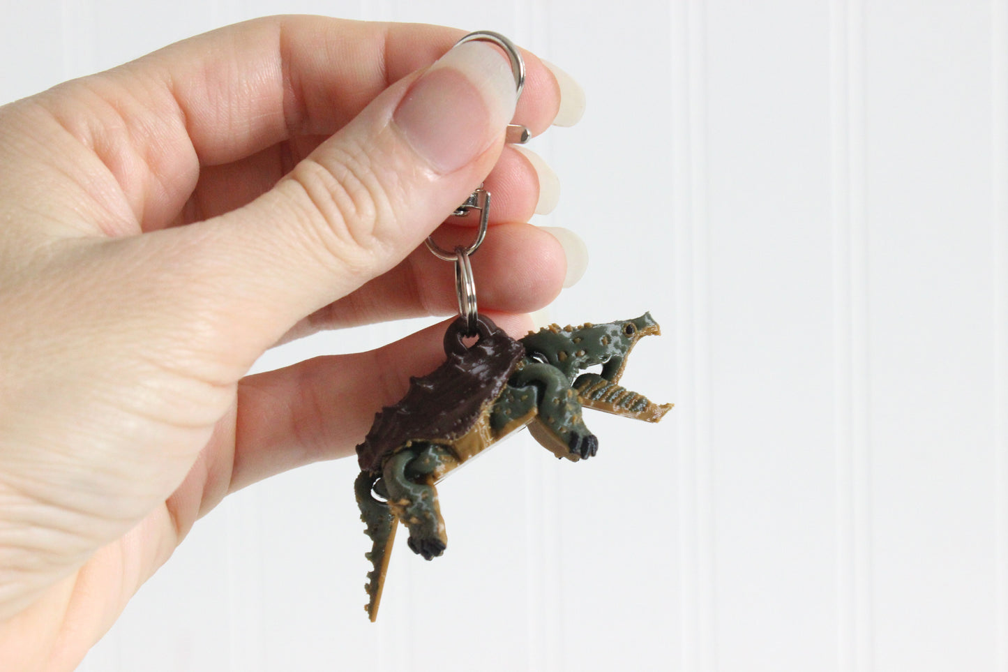 Hand holding a 3D printed alligator snapping turtle keychain showing open jaw and green textured body with swivel quick-clip key ring